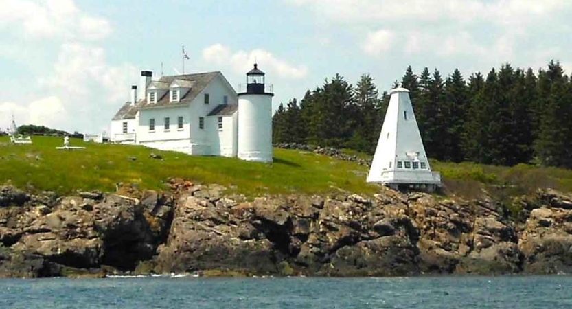 Water meets a rocky shore near a white lighthouse 